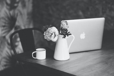 茶杯旁花瓶和桌上MacBook上花瓣的选择性聚焦和灰度摄影